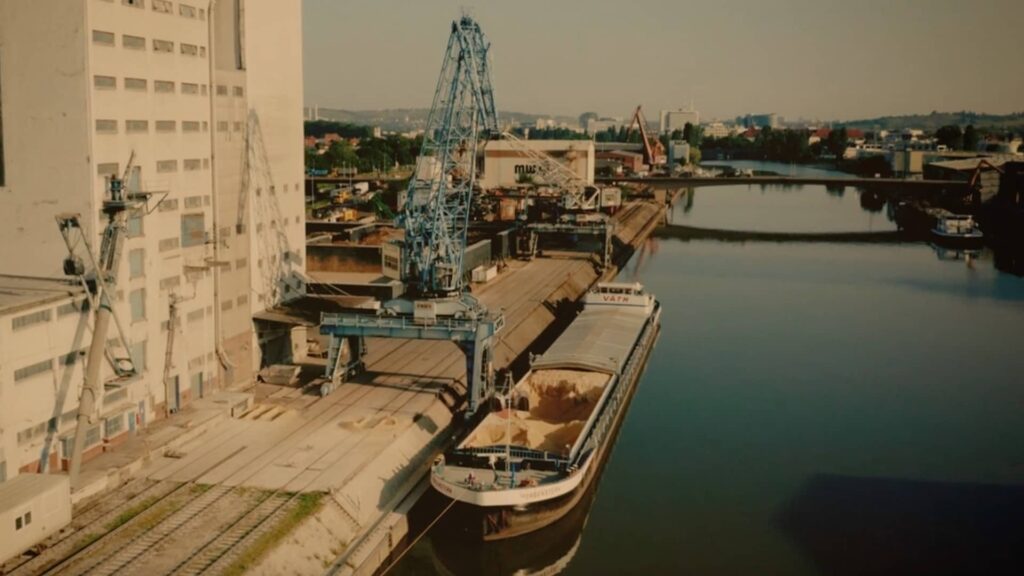 Frachtschiff mit Schüttgut am Kai eines Industriehafens mit Krananlagen und Lagergebäuden.